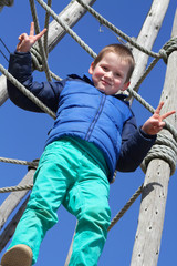 Glücklicher Junge auf Spielplatz, Klettergerüst zeigt Peace-Zeichen