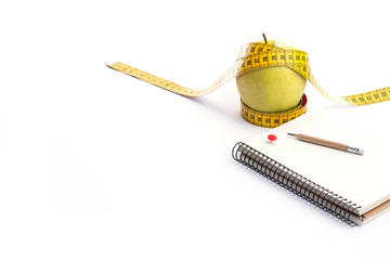 Fresh and green organic apple with metering tape and notebook on white