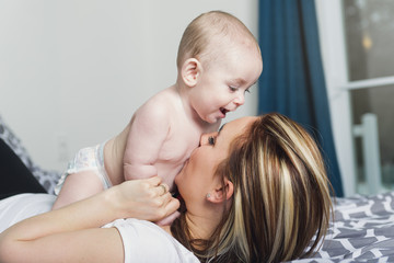 Portrait of happy young mother with a baby in the bed at home
