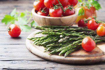 Uncooked asparagus with tomato on the wooden table