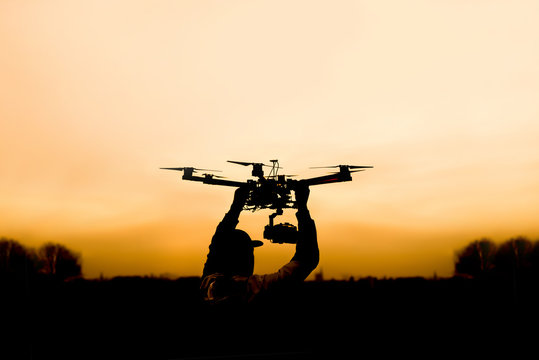 Man holding the drone, preparing for take off. Silhouette against the sunset sky.
