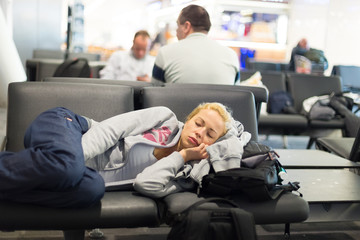 Tired female traveler sleeping on the airpot departure gates bench with all her luggage by her...