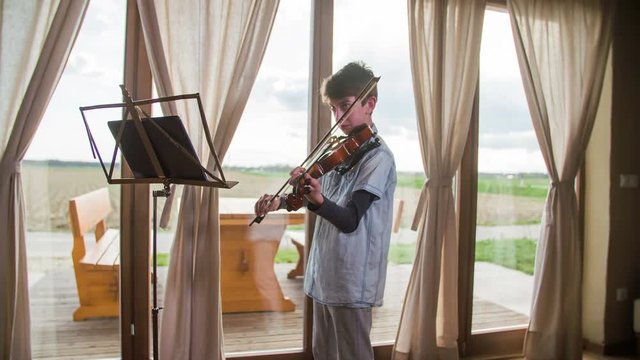 Young violinist playing in front of windows with terrace outside