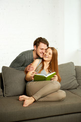 Obraz premium Young Couple Reading a Book On Sofa
