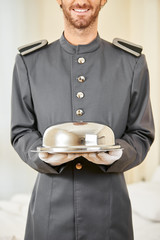 Freundlicher Page serviert Essen mit Speiseglocke