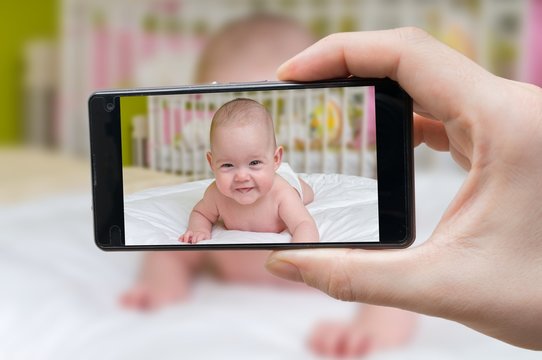 Parent is taking photo of a baby with smartphone.