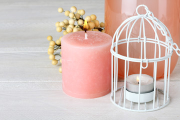 a lighted candle near the cage and vases on wooden background