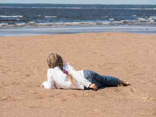Fototapeta na wymiar little blonde girl resting on the sand beach looking to the sea