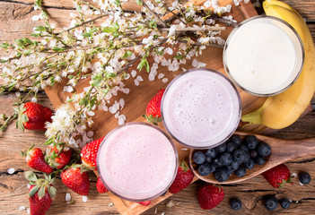 Fresh milk, strawberry, blueberry and banana drinks on wooden table, assorted protein cocktails with fresh fruits.