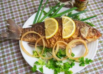 Roasted carp fish with greens on a white plate.