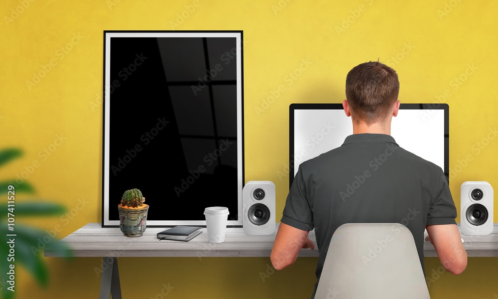 Poster man work on computer. poster frame beside. coffee, cactus, speakers on table. free space on wall for