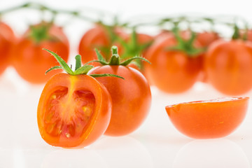 Heap of cherry tomatoes closeup and some cut in half, on white background.