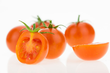 Some cherry tomatoes, one cut in half, on white background.