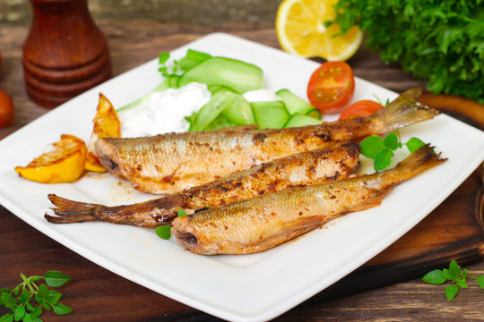 Roasted sardines with a salad of cucumber and yogurt on a wooden background. Mediterranean cuisine