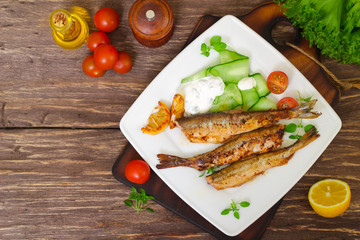 Roasted sardines with a salad of cucumber and yogurt on a wooden background. Mediterranean cuisine