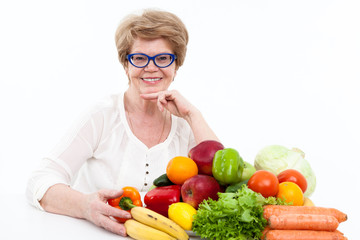 Portrait of smiling senior Caucasian woman with fresh vegetables and fruits on table, isolated on white background