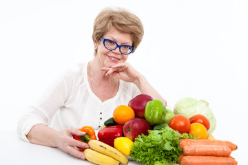 Portrait of happy elder Caucasian woman with fresh vegetables and fruits on table, white background