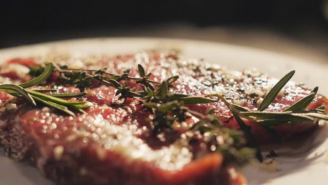 Cook puts the leaves of rosemary on the raw marinated steaks