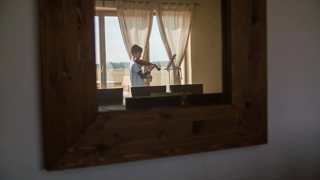 Boy play violin in mirror on wall jib shot