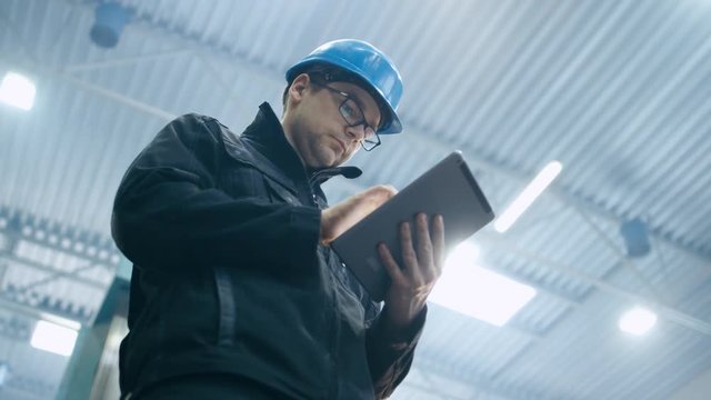 Factory worker in a hard hat is using a tablet computer. Shot on RED Cinema Camera.