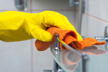 Closeup of woman's hand in yellow glove cleaning bath shelf