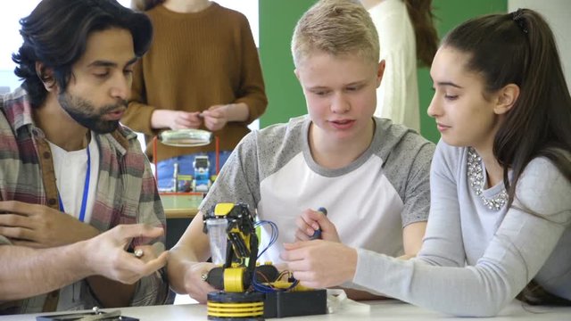 Young, male teacher helping his students build a robotic arm.