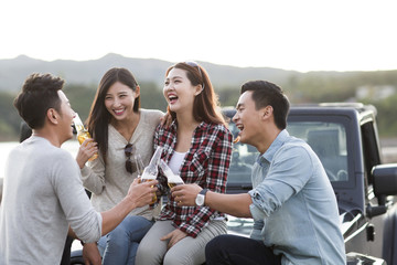 Happy friends drinking beer on a jeep