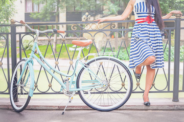 Fototapeta na wymiar Young girl standing near fence near vintage bike at park