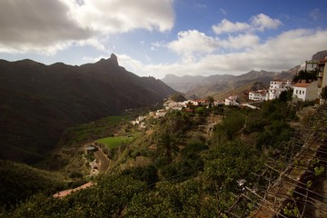 Fototapeta na wymiar Mountain small village with foggy mountains, hills and rock monument on the background. Spring. Spain - Gran Canaria.