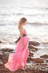 Pregnant woman in pink dress on the beach near sea