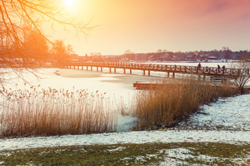 Winter frozen lake with wooden bridge at sunset light