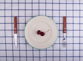 Vintage knife, fork and plate of cherry on  blue and white check