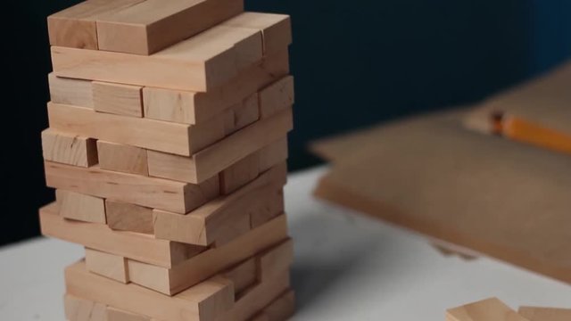 Closeup hand girl take one block on the tower from wooden blocks, dark tone.