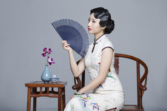 Young beautiful woman in traditional cheongsam with folding fan