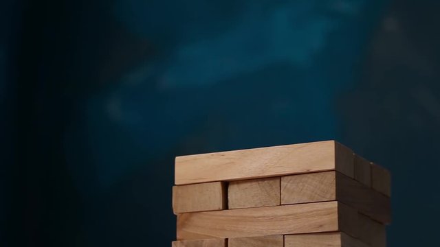 Closeup hand girl take one block on the tower from wooden blocks, dark tone.