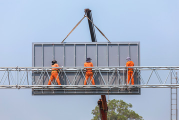 workers install big steel billboard over highway