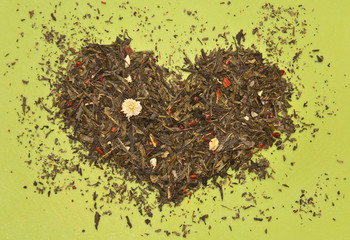 Mixture of green tea leaves and dried fruits in heart shape isolated on light green background