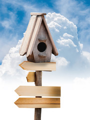 Wooden bird house on the wooden sign with blue sky with clouds.