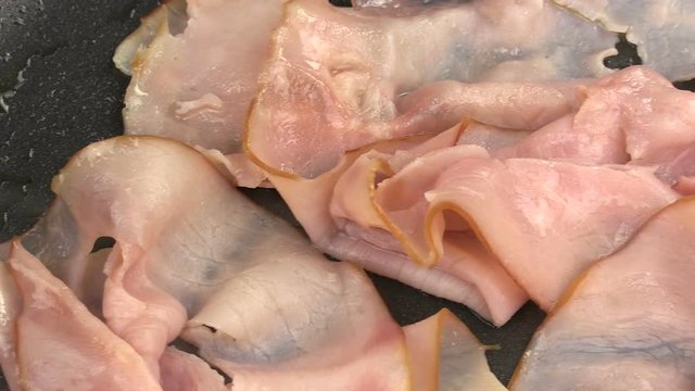 
Close up pan across slices of ham being fried in a pan.
