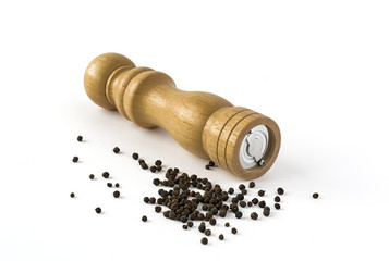Wooden pepper mill with scattered whole pepper isolated