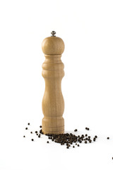 Wooden pepper mill with scattered whole pepper isolated