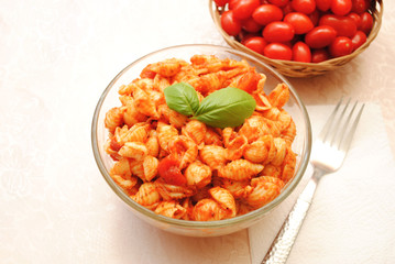 A Bowl of Vegetarian Shell Pasta with Whole Cherry Tomatoes in the Background