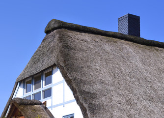 Thatched roof house, thatched cottage and blue sky. Detail shot of a cottage with thatched roof in the sun. Copy space.