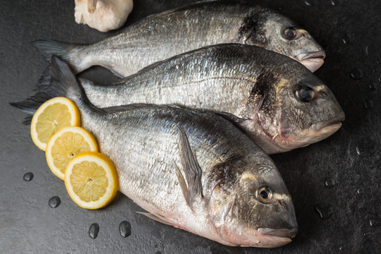 Orate pescate ed eviscerate posate su un tavolo con fettine di limone