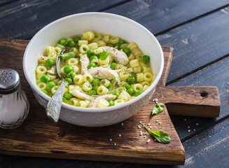 Chicken soup with pasta and green peas on a dark wooden board. Delicious healthy food