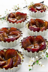 Raw tartlets with plums on white wooden background
