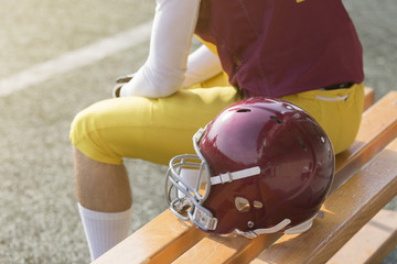 American football player sitting on bench and helmet next to him