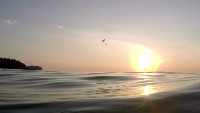 View from sea on skydiver gliding during dawn