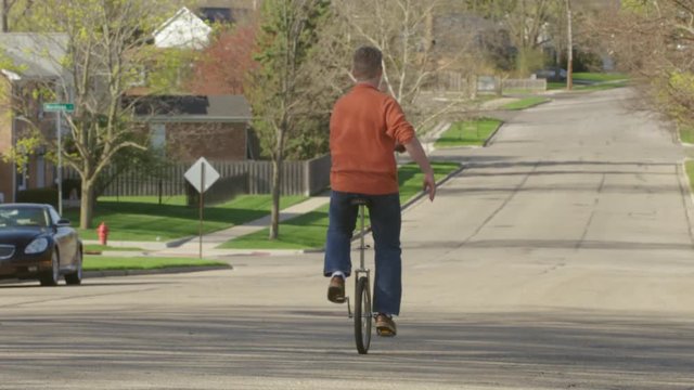 Young man riding a unicycle away down a suburban street on a sunny spring day in the American Mid West.  Recorded in slow motion 4K at 60fps.