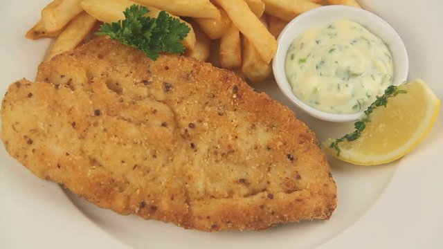 Serving a fried fish fillet with hot chips and tartare sauce garnished with parsley.